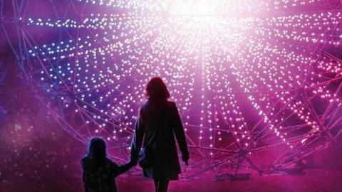 Silhouette of a woman and a small child in front of a circular light installation of hundreds of small lights
