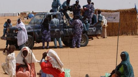 Refugees wait to get into a water station watched by armed police at the Abu Shouk camp near El Fasher in the Darfur region of northern Sudan, Tuesday August 24, 2004