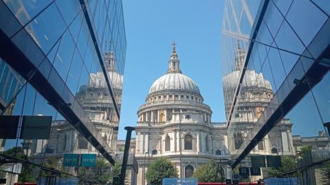 St Paul's Cathedral, seen though the gap between two large glass buildings, sits under bright blue sky