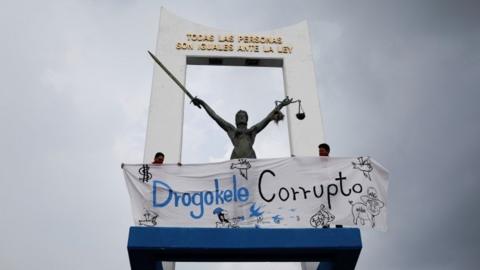 People hold a banner next to a monument, as they protest against the removal of Supreme Court judges and the Attorney General by Salvadoran congress, in San Salvador, El Salvador, May 2, 2021