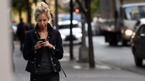 A woman uses her smartphone as she walks in New York, 13 November 2014