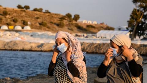 Two women wear their protective masks as they walk near the new temporary camp at Kara Tepe