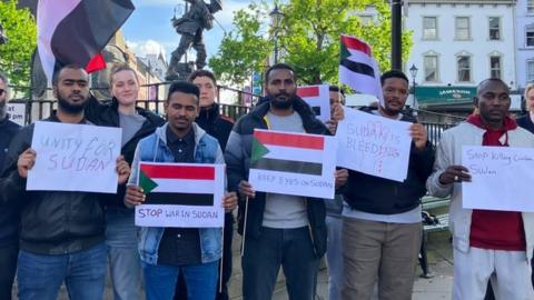 Men and women hold placards and flags at a vigil for the Sudanese community in Londonderry