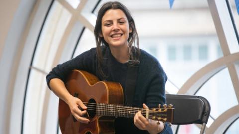 Performer Maya smiles while playing a guitar