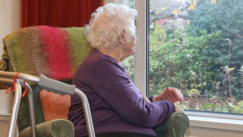 An old woman on her own looking out the window