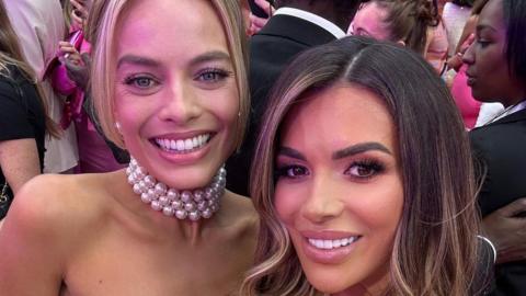 Ekin-Su Cülcüloğlu and Margot Robbie smiling for a selfie at the Barbie premiere in London. Margot has a pearl necklace on and has her blonde hair tied up while Ekin-Su has her brunette hair down