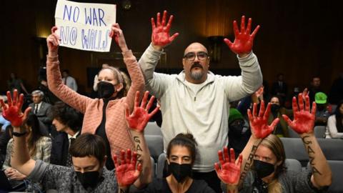 Protesters raise red painted hands as US Secretary of State Antony Blinken and Defense Secretary Lloyd Austin testify during a Senate Appropriations Committee hearing on a funding request for Israel