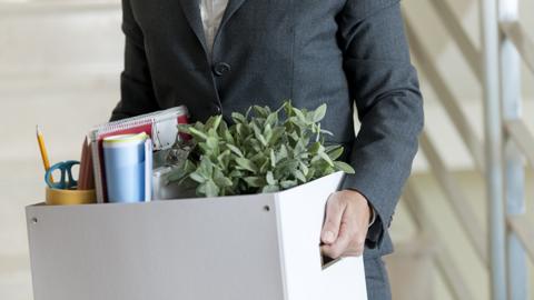 Woman in business suit carrying box out of office, having just been made redundant