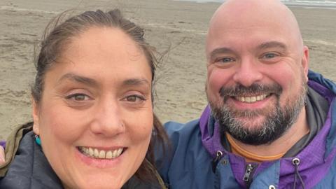 Woolsack Race organisers Kirsten and Danny Toft are pictured smiling on a beach together