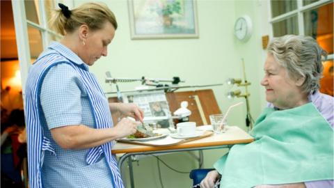 A care worker helps an elderly resident with a meal