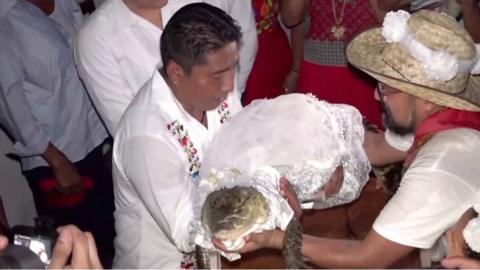 Mayor holding caiman dressed in bridal outfit