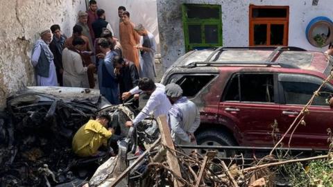 A photograph showing the destroyed car and damage around it