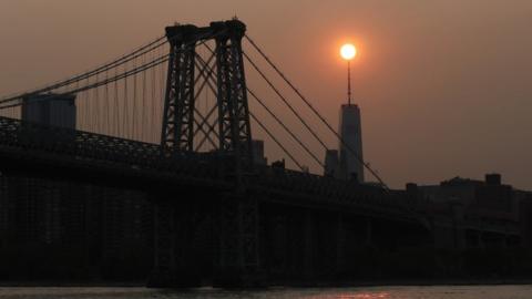 The sun sets behind the Manhattan Bridge and One World Trade Center in a haze created by smoke from the West Coast wildfires on September 15, 2020 in New York City .