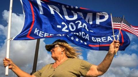 A supporter of Donald Trump holding flags near the Mar-a-Lago estate in Palm Beach, Florida