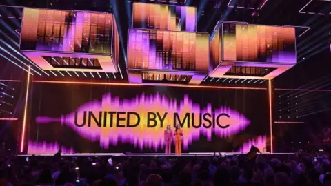 The stage at the Eurovision Song Contest is shown from a distance, with the words, "United By Music", written on the backdrop of the main stage.
