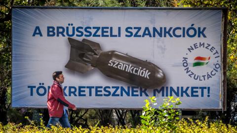 A man passes by posters depicting a bomb reading "We are being punished by the Brussels sanctions", in Budapest on October 18, 2022