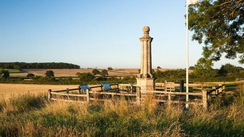Stone column with dome at the top surrounded by a fence in a field