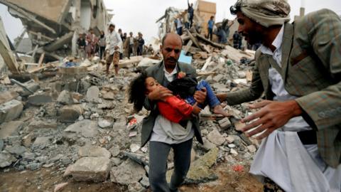 A man carries Buthaina Muhammad Mansour, a Yemeni girl rescued from the site of a Saudi-led coalition air strike that killed eight of her family members in Sanaa on 25 August 2017