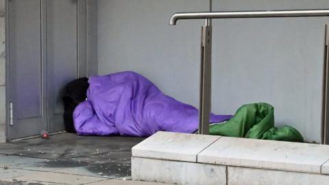 Homeless person sleeping rough in purple sleeping bag