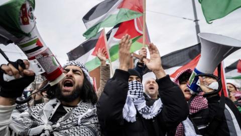 Protesters shout slogans and wave Palestinian flags during a demonstration on the day of the opening of the National Holocaust Museum