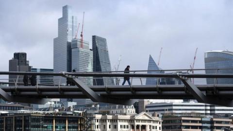 Man walking over a bridge with the City of London in the background