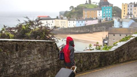 A person drags a suitcase along a street above Tenby harbour
