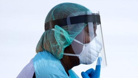 A healthcare worker points at their mask