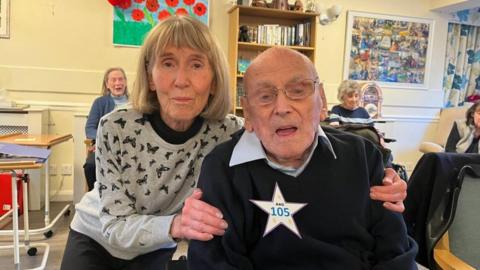 Man wearing a 105 badge and his daughter at a care home
