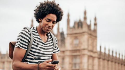 A man using a smart-phone outside the houses of parliament.