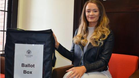 Charlotte wearing her ring next to a ballot box