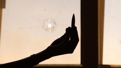 A civilian holds up an empty bullet case in front of a damaged window of a residential building during ongoing skirmish between Sudanese army and paramilitaries of the Rapid Support Forces (RSF) in Khartoum, Sudan -18 April 2023
