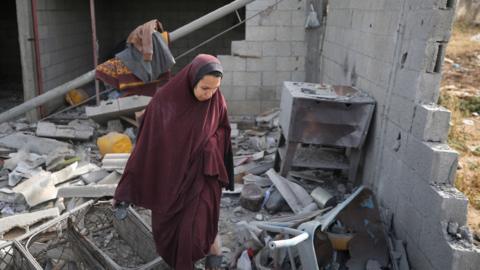 A Palestinian woman examines the rubble of collapsed apartment as Israel's attacks continue on the Gaza Strip