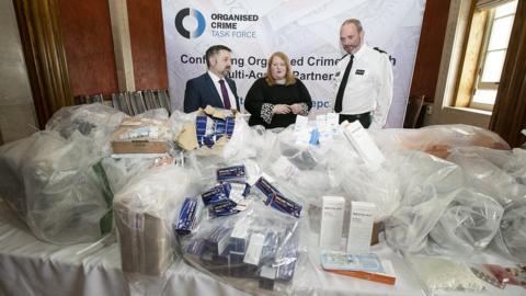 Robin Swann, Naomi Long and ACC Mark McEwan at a press conference where the seized medication was displayed