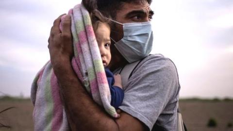 An asylum seeker holds his daughter as they await transportation to a processing centre in the US