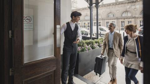 A young hotel doorman welcomes guests to a hotel