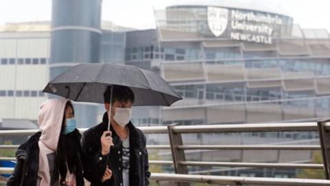 Two people wearing face masks walking together with a Northumbria University building seen in the background