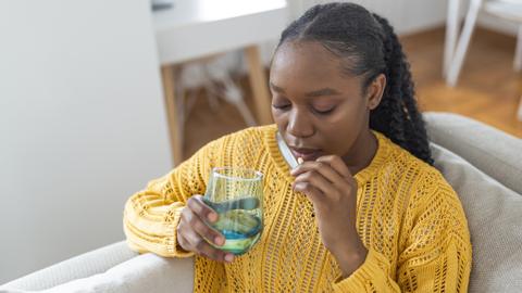 Woman taking antibiotics at home, wearing a yellow jumper with a glass of water