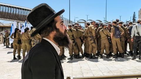 An ultra-Orthodox man walks past Israel soldiers