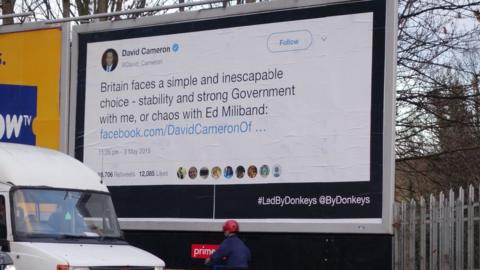 A tweet by former Prime Minister David Cameron reading "Britain faces a simple and inescapable choice - stability and strong Government with me, or chaos with Ed Miliband" is on a billboard next to the A10 in London