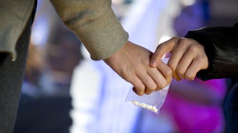 A stock image showing a clear bag containing drugs being exchanged