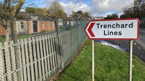 Road sign for Trenchard Lines in front of the army residences which are red brick and behind a large wire fence with barbed wire at the top.