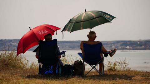 People sheltering under umbrellas from the sun in St Michael's Bay in Cornwall. Temperatures are predicted to hit 31C across central England on Sunday ahead of record-breaking highs next week. Picture date: Sunday July 17, 2022.
