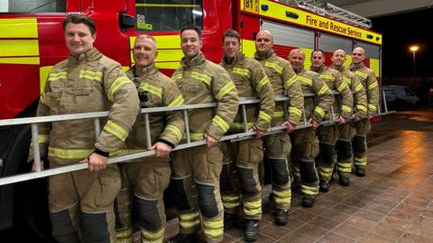 Nine firefighters holding a ladder