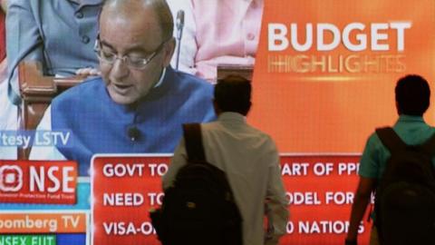 Indian office-goers walk past a screen showing Indian Finance Minister Arun Jaitley delivering his 2015 Budget speech on February 28, 2015