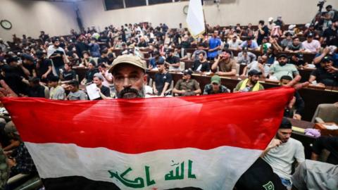 A man deploys a national flag as supporters of the Iraqi cleric Moqtada Sadr gather inside the country's parliament in the capital Baghdad's high-security Green Zone