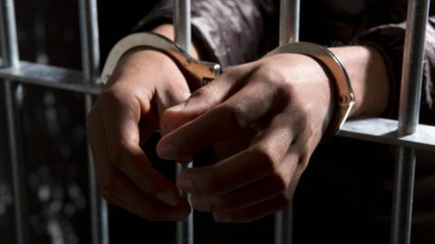 Handcuffed hands seen behind prison bars