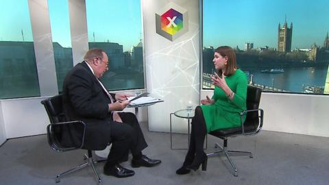 Andrew Neil consults his papers as Jo Swinson gestures, overlooking a view of the Thames in London with Parliament visible in the background