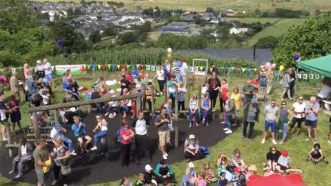 A crowd of people gathered watching a band play in the park