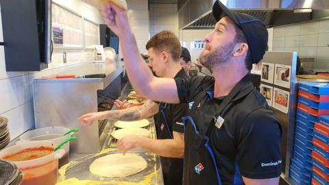 A Domino's Pizza cook flips dough in the air