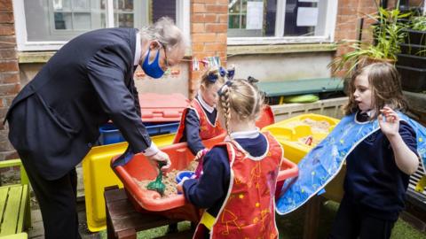 Education Minister Peter Weir and three schoolgirls plays in a sandpit in a school